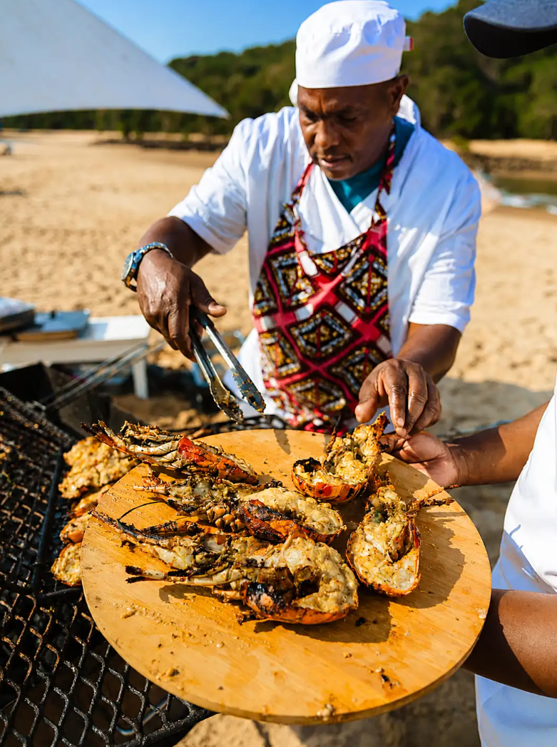 Bemugi's chef plating freshly grilled lobster and prawns on the beach